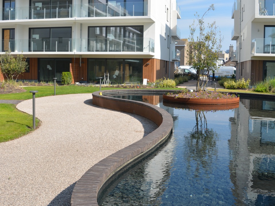 Moderne tuin met waterpartij en groenvoorziening bij residentieel gebouw, aangelegd door Castelein Landscaping