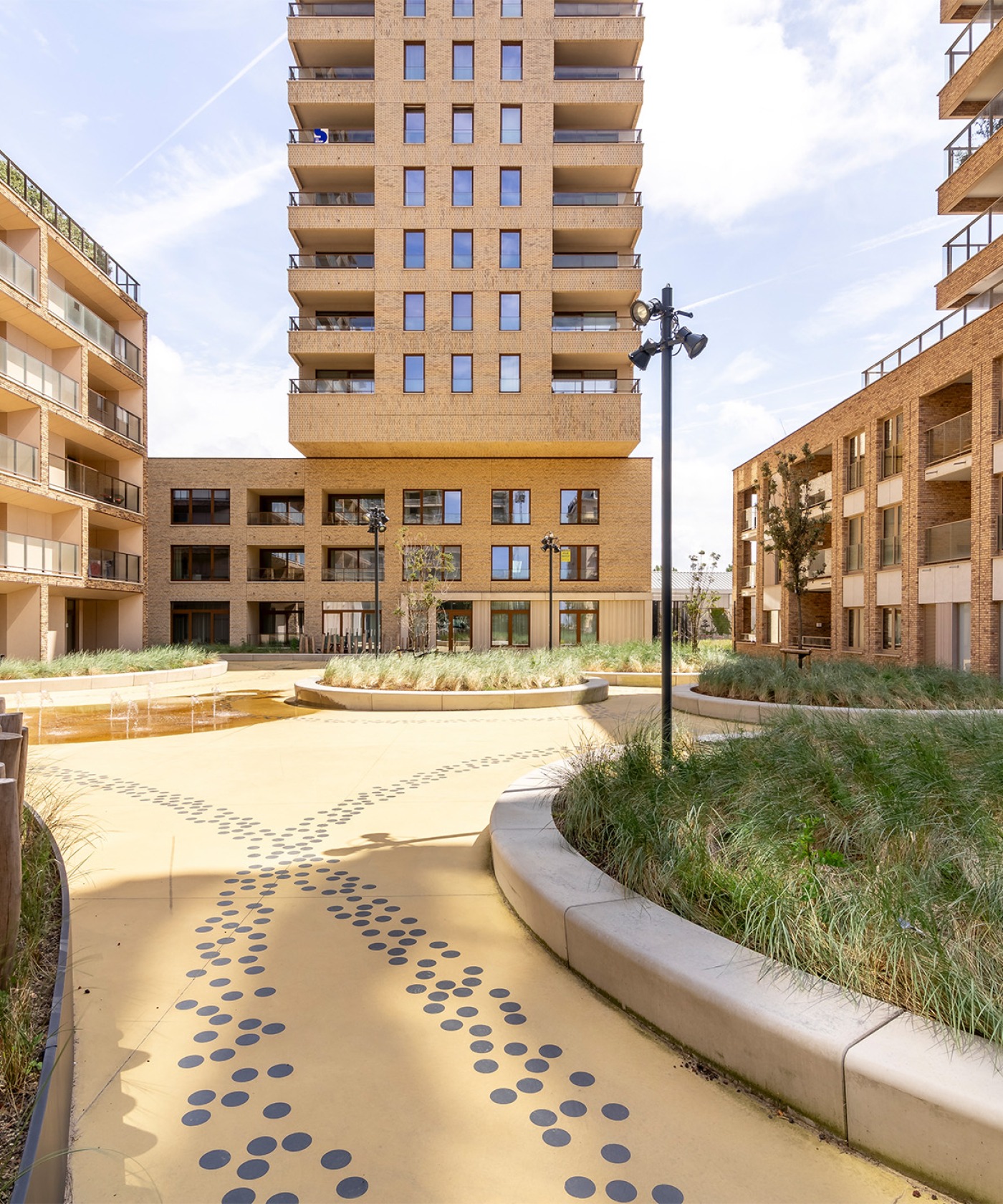 Grote binnentuin met groene eilanden, houten ligbanken en fonteinen bij O'Sea wooncomplex, Oostende